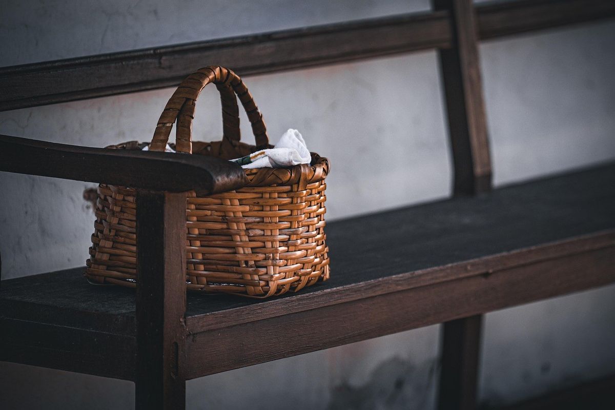 Panier en osier posé sur un banc en bois, contenant un objet blanc, contre un mur gris