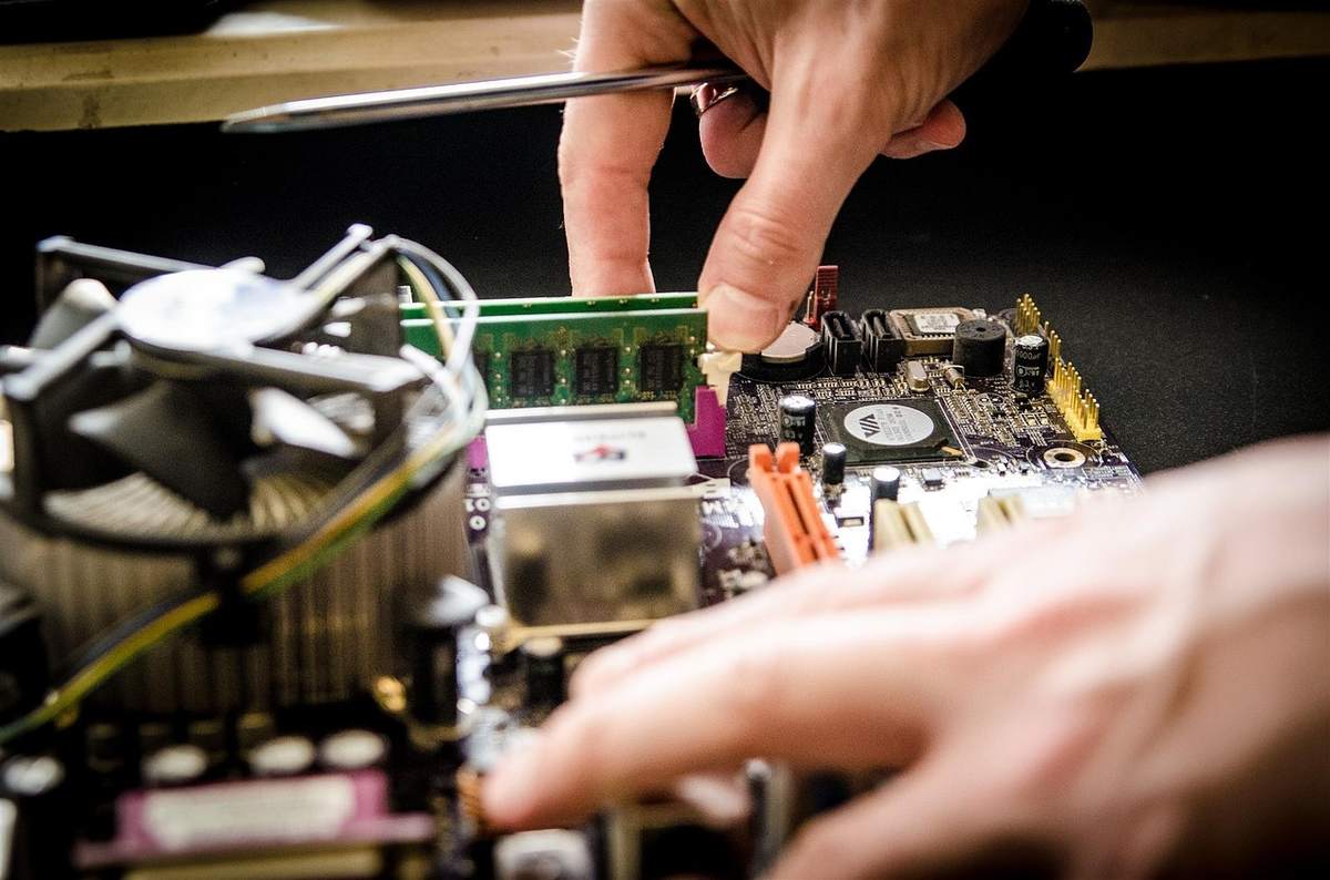 Une main installe une barrette RAM sur une carte mère avec un ventilateur Une main installe une barrette RAM sur une carte mère avec un ventilateur