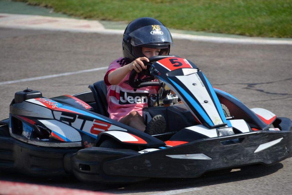 Un enfant en karting sur circuit, portant casque, pilotant go-kart rouge