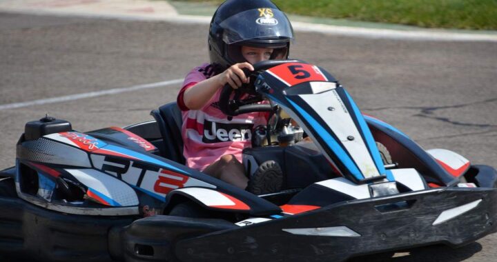 Un enfant en karting sur circuit, portant casque, pilotant go-kart rouge